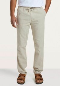 Lichtbeige linnen broek met een elastische tailleband en een trekkoord, met een relaxte pasvorm en zijzakken. Gecombineerd met bruin slippers.