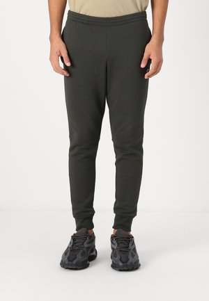 Pantalons de survêtement vert foncé avec taille élastique, coupe ajustée et chevilles resserrées, associés à des chaussures de sport noires à motifs.