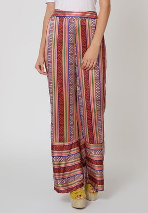 Pantalones de pierna ancha rojos y estampados con rayas, que presentan diseños geométricos. El material tiene una textura suave. Se llevan con zapatos de plataforma amarillos.