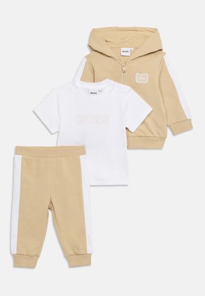 Beige en wit peuterdrie-delig setje met een zip-up hoodie, een T-shirt met korte mouwen en "BOSS"-logo, en een broek met elastische taille en witte zijstrepen.
