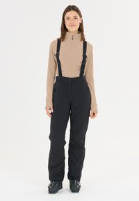 Sorte skibukser med justerbare seler, sidelommer og en glat tekstur, parret med en beige langærmet top.