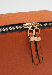 Borsa in pelle arancione con texture, dotata di doppia cerniera con dettagli in metallo color oro e accenti neri, evidenziando l'artigianato e i dettagli del design.