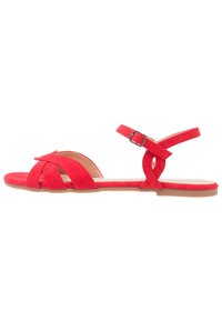 Sandale en daim rouge à bout ouvert, avec des brides croisées et une bride de cheville avec boucle. Semelle plate et design minimaliste.