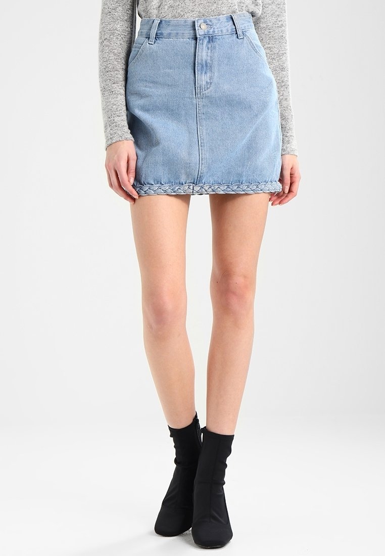 Jupe en denim bleu clair, avec une taille haute, un ourlet tressé et une silhouette près du corps. Associée avec des bottines noires.