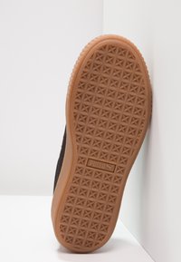 Brun gummisula med ett stjärnmönster. Svart texturerad ovandel synlig längs sidan, med en märkesetikett.