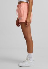 Persika bomullsblandning shorts med ett elastiskt midjeband, sidofickor och vit broderad logotyp. Tillsammans med vita sneakers och ankelsockar.
