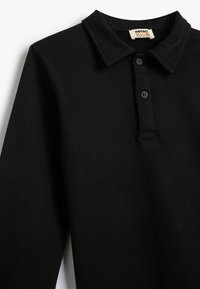 Zwarte polo met lange mouwen, gemaakt van zachte stof, met een kraag, drie-knopen sluiting en minimale stikdetails.