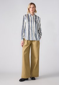 Camicia a righe bianca, blu navy e blu; abbinata a pantaloni khaki a vita alta e gamba larga; scarpe slip-on nere.