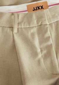 Beige katoenen broek met een gladde textuur, voorzien van een centrale plooi, zijzak en een gelabeld bruin etiket op de tailleband.
