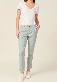 Světlé zelené bavlněné chinos kalhoty s ohrnutými nohavicemi, klasický střih, se zapínáním na jeden knoflík, předními kapsami a v kombinaci s bílým tričkem s výstřihem do V.