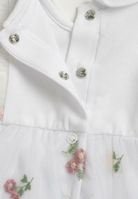 Vêtements pour bébé blancs avec des boutons-pression et des fleurs roses brodées avec des feuilles vertes en tissu tulle doux.