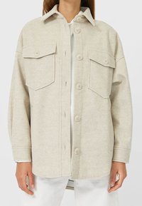 Beige wollen overhemdjacket met twee voorzakken, knoopsluiting en een klassieke kraag. Zachte, textuurvolle stof met een ontspannen pasvorm.