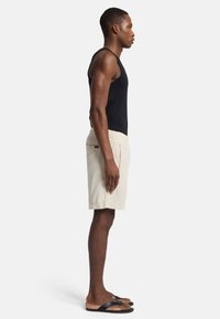 Zwarte tanktop, romige shorts met elastische tailleband en zijzak, en zwarte flip-flops. Focus op minimalistisch casual design en pasvorm.