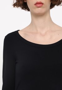 Zwarte lange mouw top met een brede halslijn, gemaakt van een zachte stof, met een gladde textuur en minimale naaddetails.