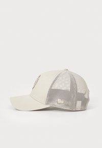 Beige caps med strukturert front, mesh bak og brodert logo. Skjermen er litt buet, med en subtil glans og teksturerte detaljer.
