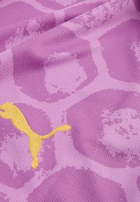 Lila atletisk tyg med ett hexagonalt mönster och en gul Puma-logga. Texturen är andningsbar med en nätliknande utseende.