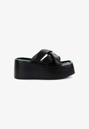 Czarne klapki na platformie z grubymi krzyżującymi się paskami i masywną podeszwą na białym tle.