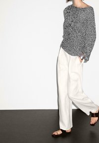 Black and white patterned long-sleeve top paired with white wide-leg trousers and brown sandals, featuring an oversized fit and relaxed style.