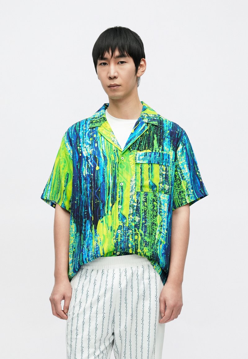 Koszula z krótkim rękawem zdobiona żywym, abstrakcyjnym wzorem w odcieniach zieleni, niebieskiego i czerni. Tkanina wydaje się lekka, a krój luźny.