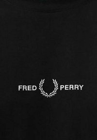 Camiseta de algodón negra con un logo bordado en blanco que presenta una corona de laurel y el texto "FRED PERRY" centrado debajo del diseño.