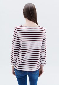 Raidallinen pitkähihainen paita valkoisena ja maroonina, jossa on pyöreä kaula-aukko, pehmeä kangas ja rento malli, yhdistettynä sinisiin farkkuihin.