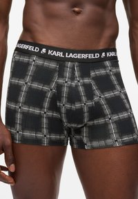 Férfi felsőtest fekete-fehér kockás boxer alsóneműben, Karl Lagerfeld logós derékrésszel, egy sima fehér háttéren.