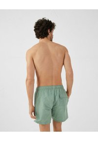 Groene shorts gemaakt van lichtgewicht stof, met een elastische tailleband en een achterzak. Het ontwerp is eenvoudig met een gladde textuur.