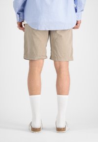 Beige šortky s volným střihem, vyrobené z lehkého materiálu, v kombinaci s bílými, žebrovanými pánskými ponožkami a světlými slip-on botami.