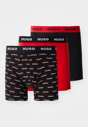 Drei Paar Boxershorts: schwarz mit rotem 'HUGO'-Muster, einfarbig rot und einfarbig schwarz. Jede hat einen schwarzen Gummibund mit 'HUGO'-Logo.