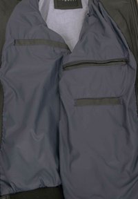 Schwarzes Jackeninneres mit glattem, dunkelgrauem Futter. Verfügt über zwei mit Reißverschluss verschließbare Taschen und eine offene Tasche. Minimalistisches Design, ohne Muster.