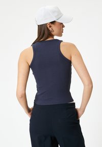 Camiseta sin mangas de canalé en color marino con un diseño ajustado, que cuenta con tirantes anchos y un dobladillo curvado, combinada con pantalones oscuros y una gorra blanca.