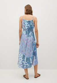 Maxikleid mit verstellbaren Spaghettiträgern, in Hellblau mit Paisleymuster. Fließender Stoff und taillierter Schnitt. Braune Sandalen sichtbar.
