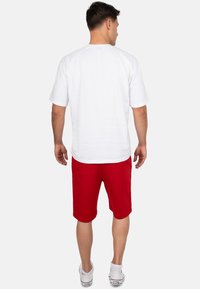 Witte T-shirt met korte mouwen, gecombineerd met rode shorts, met een ontspannen pasvorm en een zachte katoenen textuur. Draagt witte sneakers.