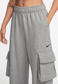 Housut harmaasta puuvillasta, joissa on joustava vyötärö, sivutaskut ja cargo-tyyliset taskut. Lantiossa on pieni musta Nike-logo.