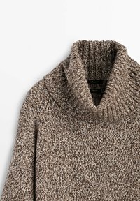 Pull en tricot marron avec un col cheminée haut et côtelé, à coupe décontractée. La texture présente un motif moucheté de fils plus clairs et plus foncés.
