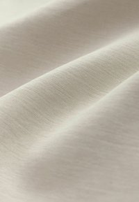 Lichtbeige stof met een gladde textuur, voorzien van een subtiel geweven patroon en zachte val, die de buigzaamheid en het gewicht benadrukt.