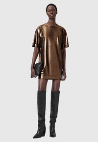 Bronsmetallisk oversized klänning med korta ärmar och rundad halsringning, tillsammans med svarta knähöga klackstövlar och en liten svart clutch.