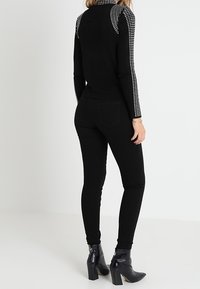 Mustapaita pitkillä hihoilla, jossa on hopeiset strassikoristeet olkapäillä, yhdistettynä tiukkoihin mustiin housuihin ja mustiin korollisiin nilkkabootseihin.