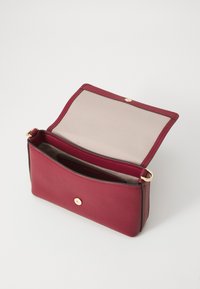 Rote Lederhandtasche mit glatter Textur, einem goldfarbenen Druckknopfverschluss und einem beigen Innenfutter. Offenes Design, das das Innenfach zeigt.