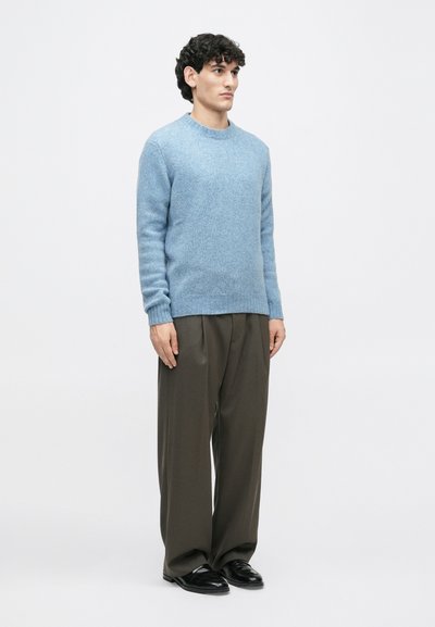 Gai zils vilnas džemperis ar apaļu kakla izgriezumu, ribotām piedurknēm un ķermeni. Valkāts ar tumšām, vaļīgām biksēm un melniem apaviem.