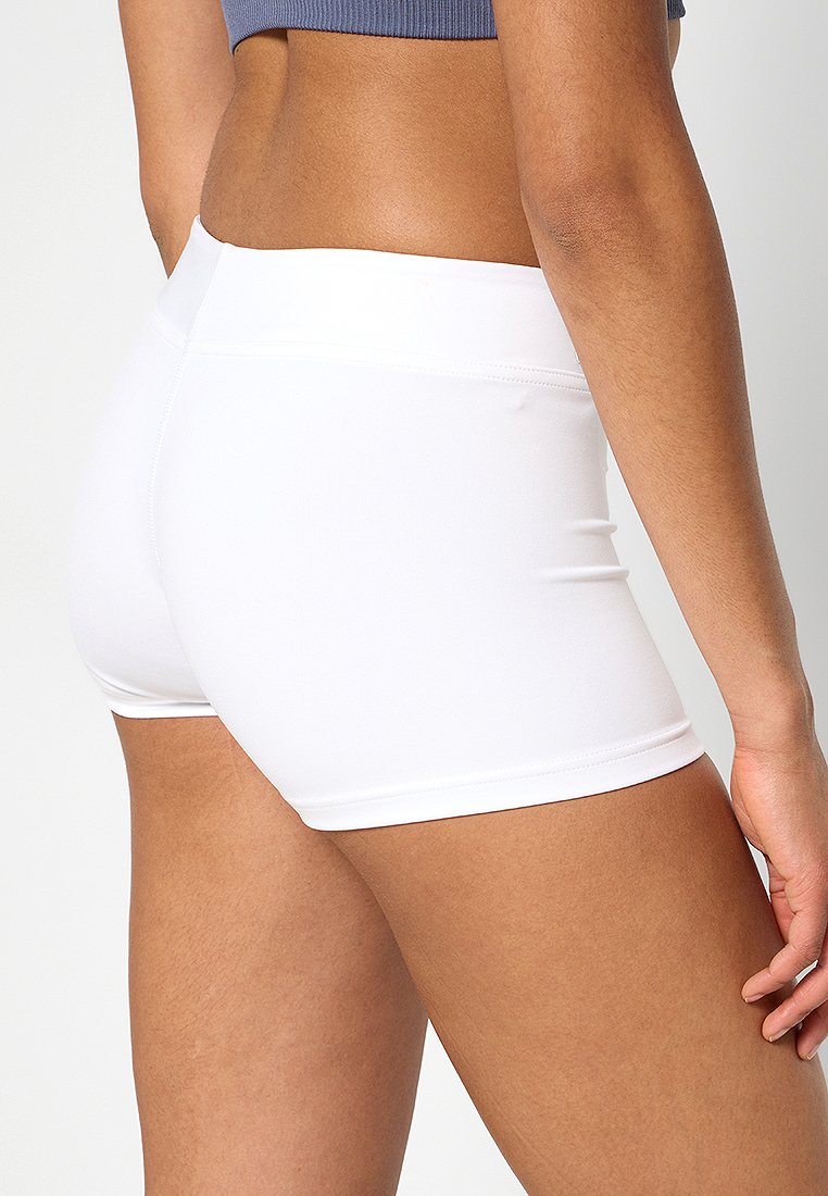 Frau in weißen, eng anliegenden Sportshorts und einem blauen, kurzen Oberteil, von hinten auf Taillen- und Oberschenkelhöhe gezeigt.