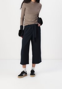 Ribbed brown long-sleeve top with a scalloped neckline, paired with black wide-leg pants with a tied waistband and black sneakers with white stripes.