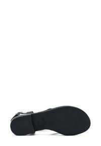 Suola di scarpa nera con una texture liscia, caratterizzata da un leggero tacco e una strap con fibbia. Logo di marca ben visibile impresso sul lato inferiore.