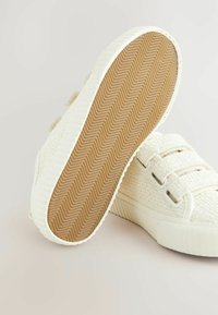 Baskets blanches avec un dessus en tissu texturé, dotées de trois sangles élastiques, de semelles en caoutchouc et d'un motif en chevron.