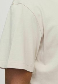 Lyse beige kortærmet t-shirt med en blød tekstur og en lige kant, der har en rund halsudskæring og subtile syninger.