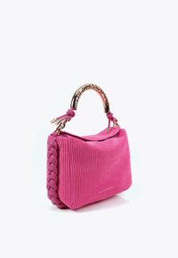 Bolso de pana rosa con lado trenzado, asa curva dorada con el nombre de la marca grabado y cierre de solapa sobre fondo blanco.