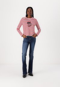 Red and white striped long-sleeve shirt with a black cartoon fox graphic, paired with blue flared jeans and black shoes.