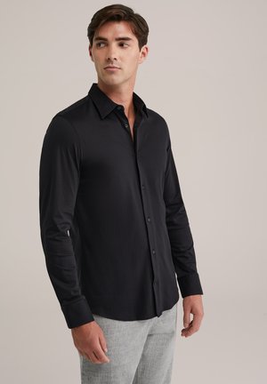 Black long-sleeve button-up shirt with a streamlined fit, pointed collar, and smooth texture, paired with light gray textured pants.