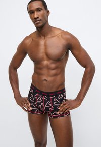 Μαύρο σλιπ με σχέδιο καραμέλας, κόκκινες λεπτομέρειες και λογότυπο στη μέση. Κατασκευασμένο από ελαστικό ύφασμα για άνεση και καλή εφαρμογή.