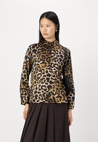 Leopard print blouse in shades of gold, brown, and black; features a collar and long sleeves, paired with a dark pleated skirt.